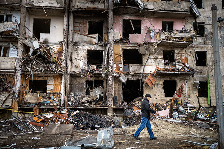 a lone man in a hat and jeans walks past a building complex shattered by Russian missiles in Kyiv, Ukraine