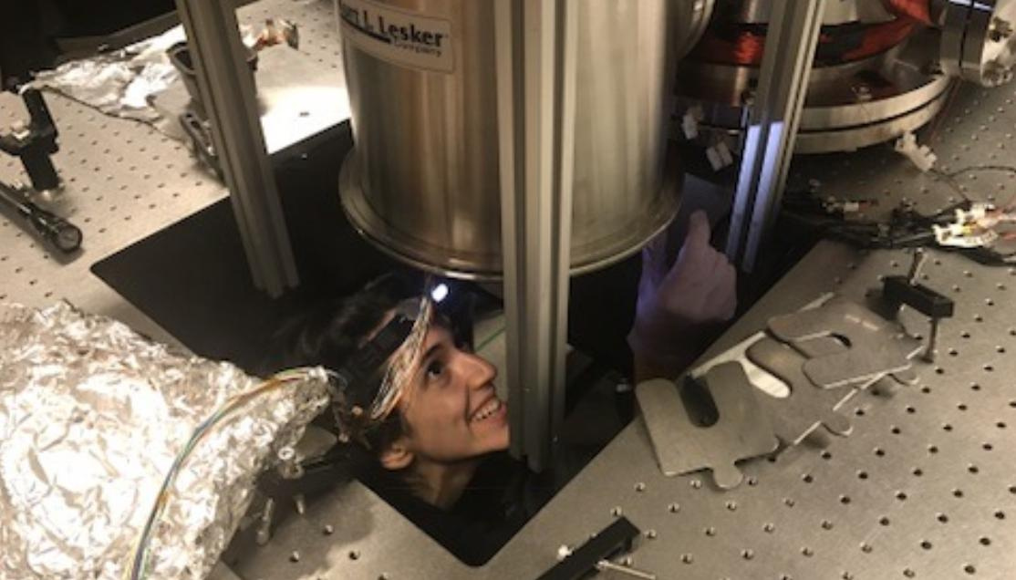 a woman's head protrudes from under the floor, where she is working on a stainless steel cylinder