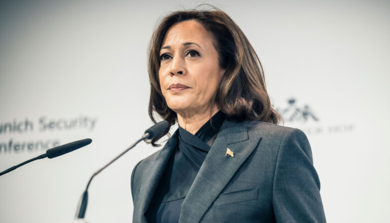 Vice President. Kamala Harris wears a serious expression as she stands before a pair of microphones