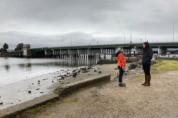 Two individuals are standing outdoors near the edge of a body of water.