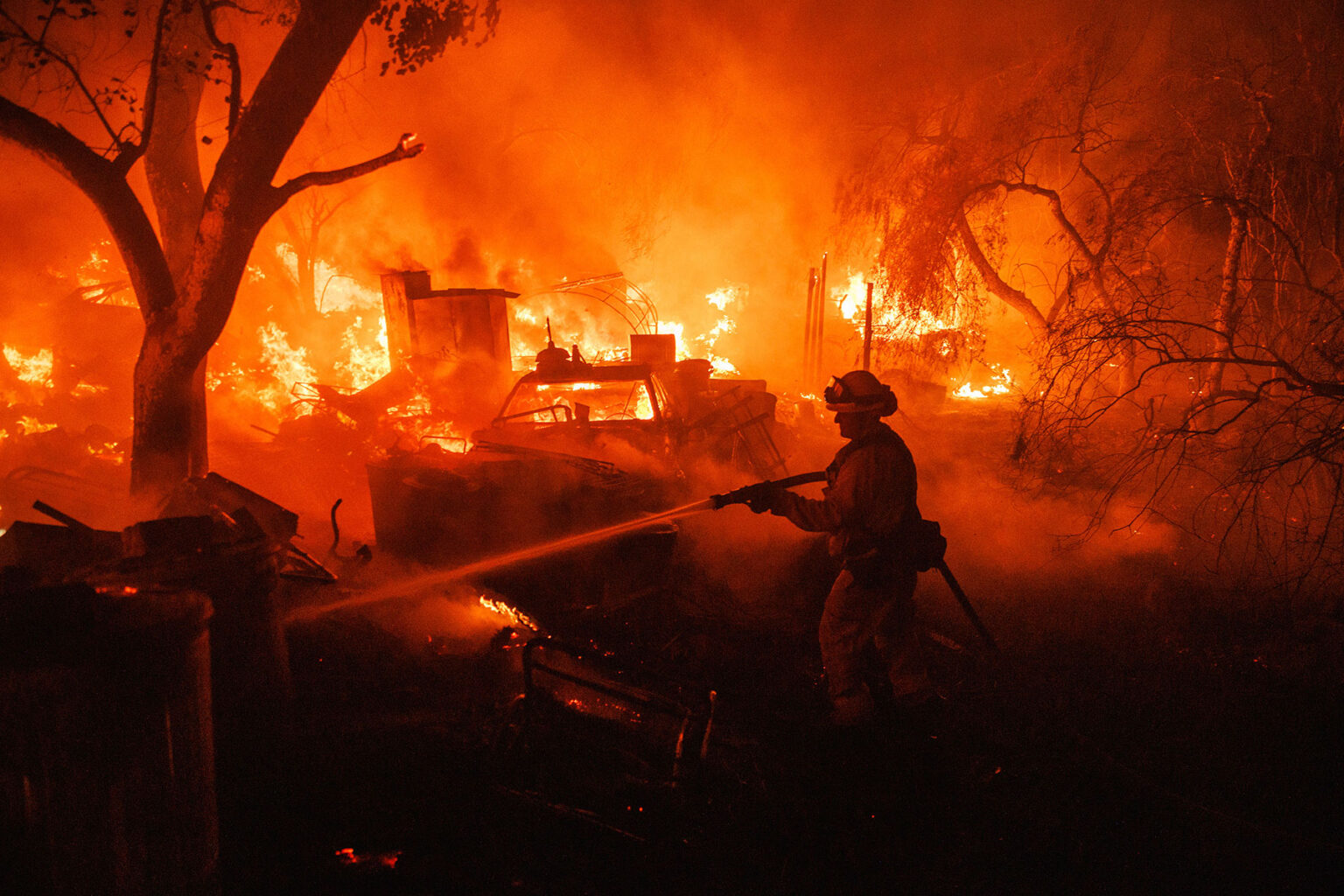 A firefighter takes a hose to a burning property while battling the Fairview Fire on Monday, Sept. 5, 2022, near Hemet, Calif.