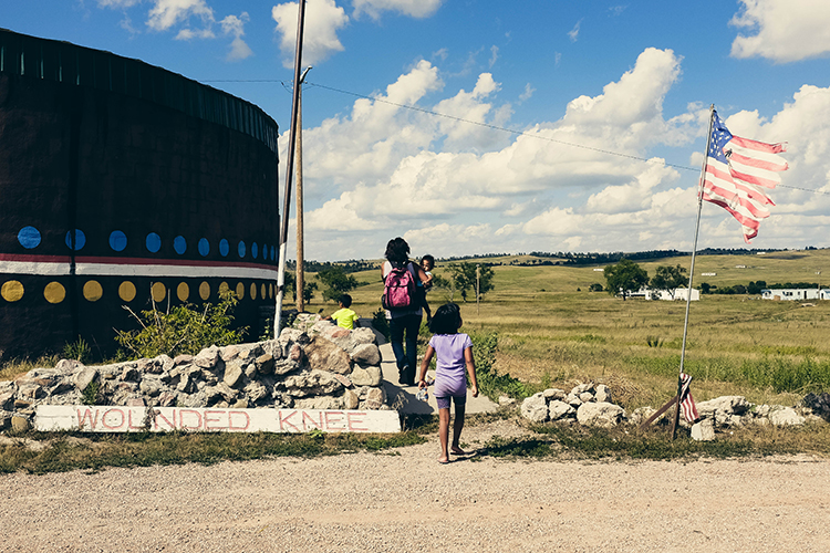 Native family walking in a field where an American flag is planted in South Dakota.