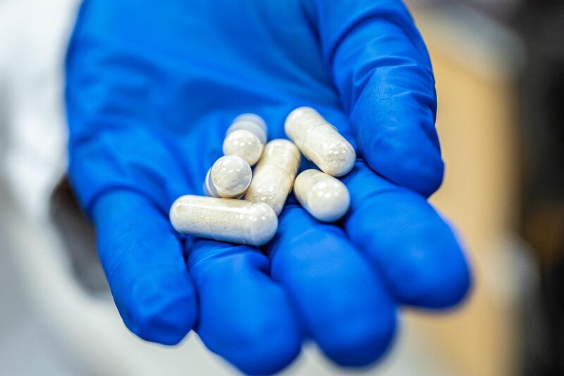 picture of a gloved hand holding white pills 