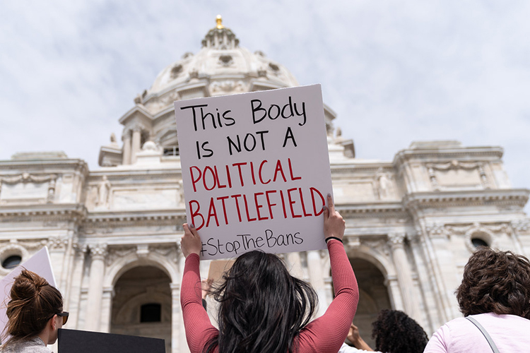 a person holds a sign that reads "This body is not a political battlefield"