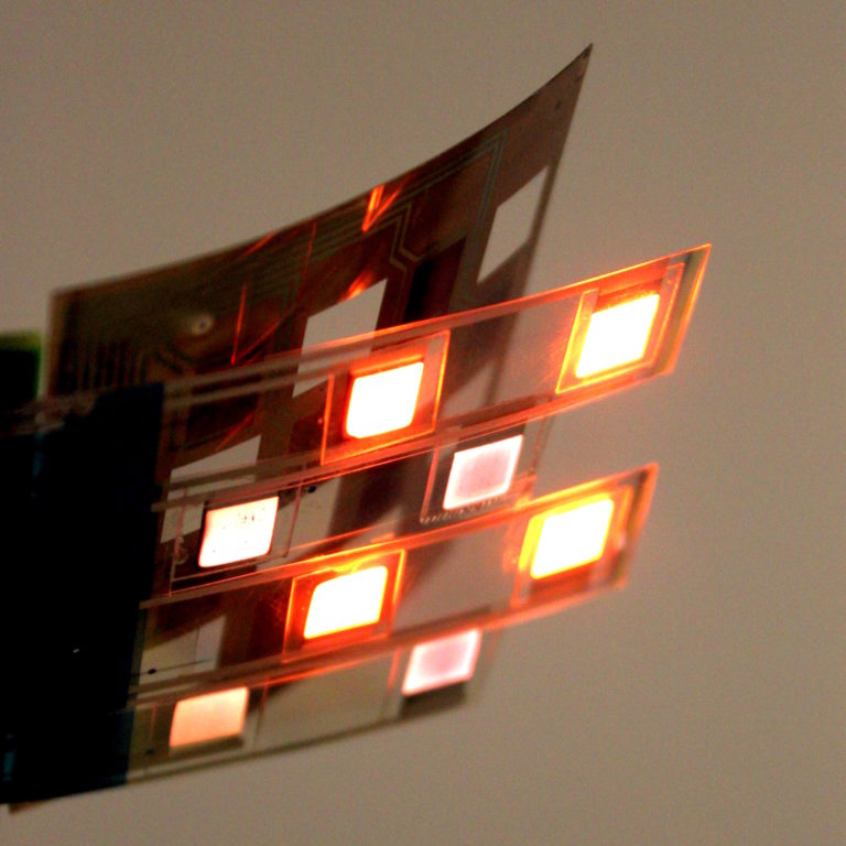 Two sheets of printed electronics, one is brown and the other is lit up with red and infrared lights. 