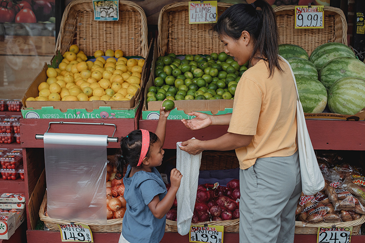 a mom and young child pick out fruit at an outdoor supermarket