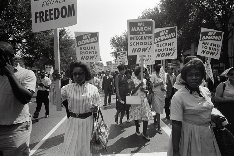 A b&w photo of a 1963 civil rights protest in which signs call for equal rights and end to bias
