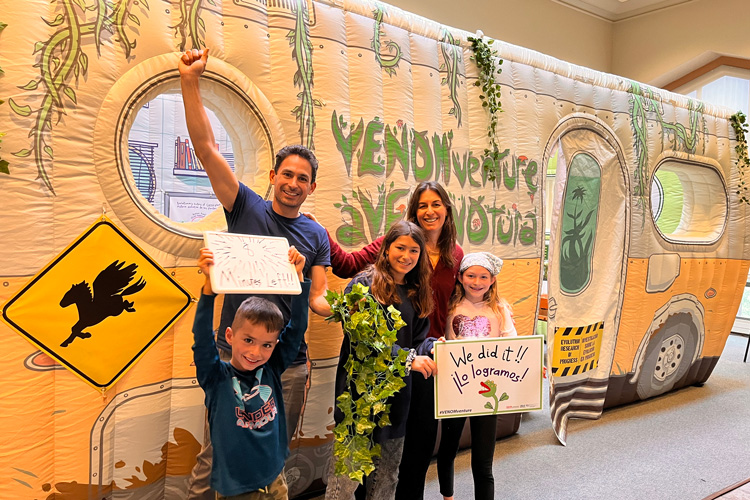 a man and woman with their three children, celebrating with raised fists their escape in front of the inflated mobile lab, colored green and orange