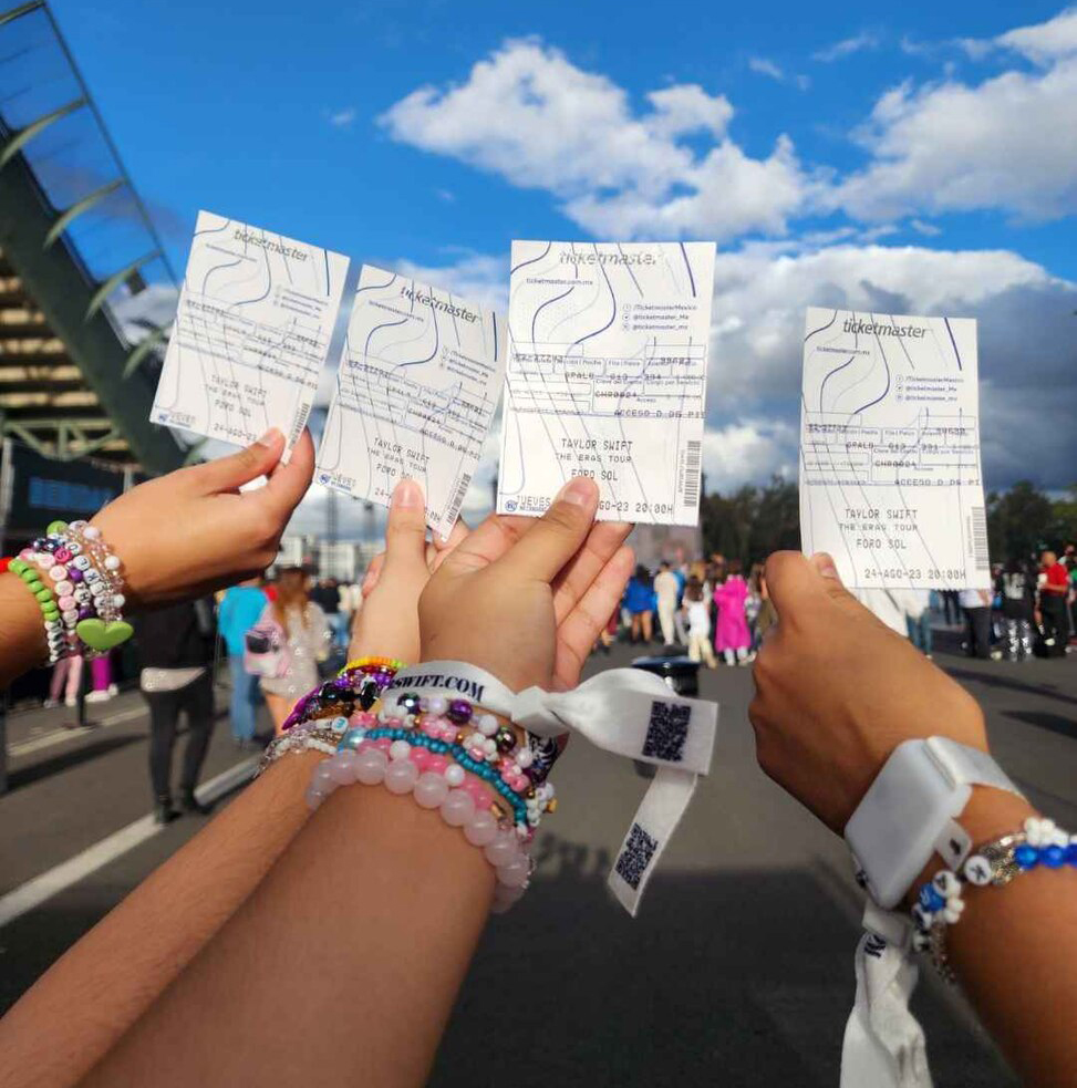 fans at a taylor swift concert wearing friendship bracelets hold up tickets to the Eras tour