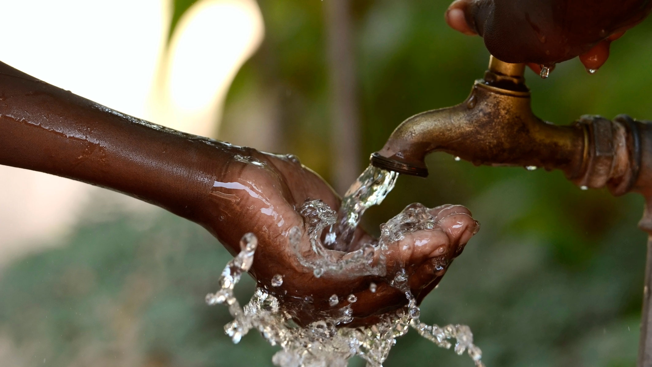 Child's hand receiving water from a spigot.