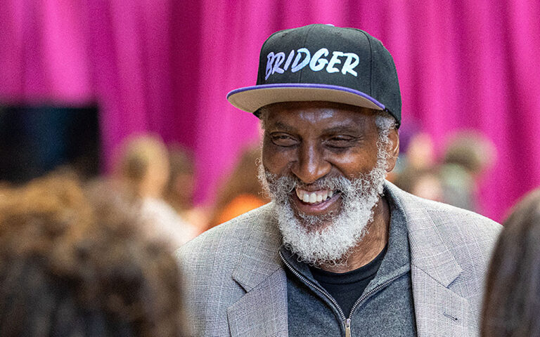 john a. powell, a civil rights scholar and founder of the Othering and Belonging Institute, smiles broadly as he wears a baseball cap that reads "Bridger"