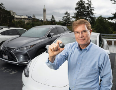 Per Peterson holding a fuel pebble in front of parked cars, with the Campanile in the background.