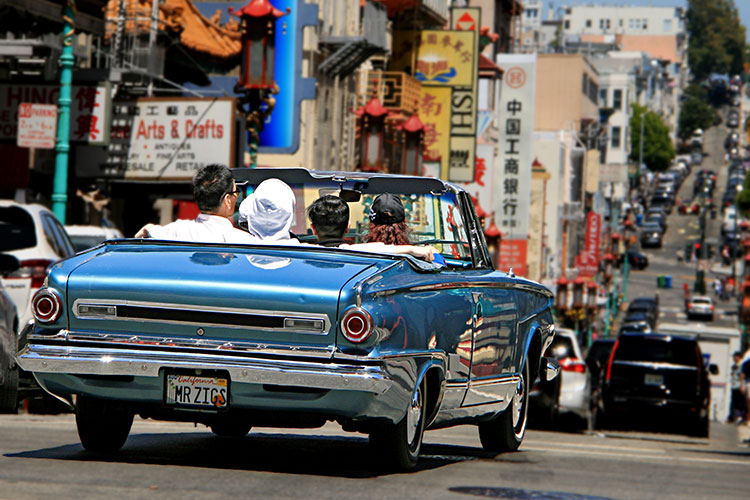 A classic convertible automobile, full of people, driving down a street in San Francisco's Chinatown district