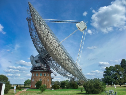 a large radio telescope sitting atop a brick building under blue skies