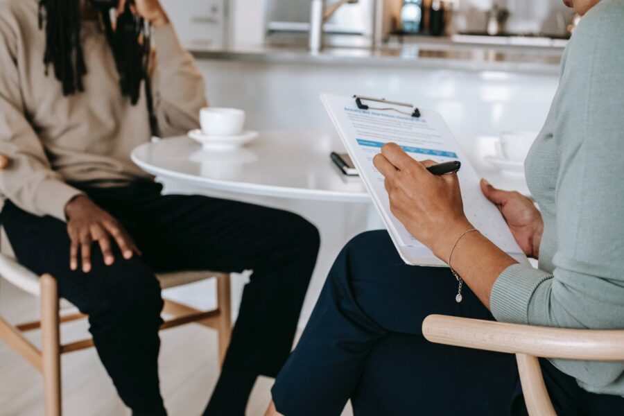 2 people sitting and talking with one of them holding a clipboard