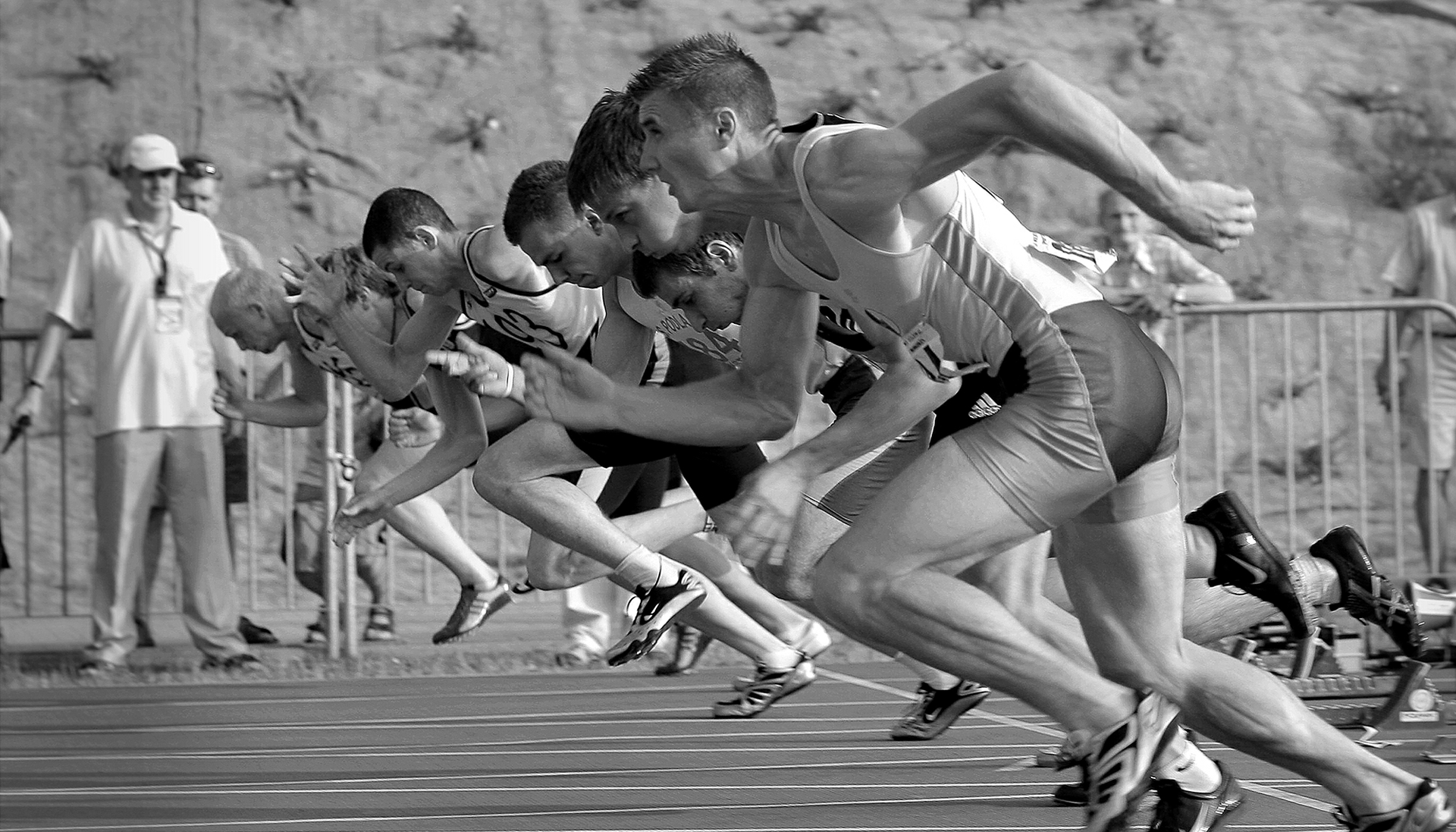 black-and-white photo of race start, showing men propelling themselves off the starting blocks