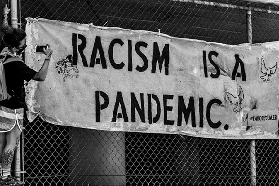 man taking picture of sign that says racism is a pandemic