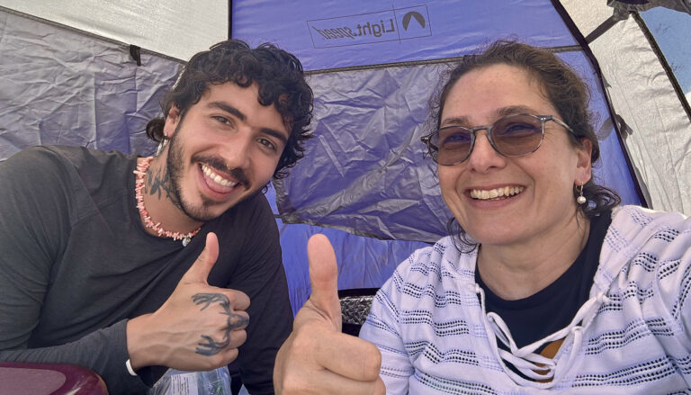 a man and woman inside a tent looking into the camera with thumbs up