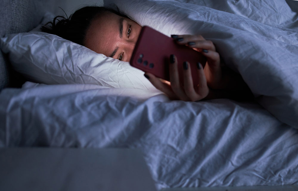 image of woman in bed on her phone