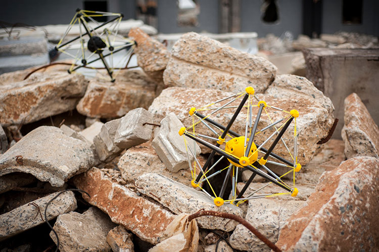 A pair of yellow, buckyball-shaped robots sit on a pile of rubble