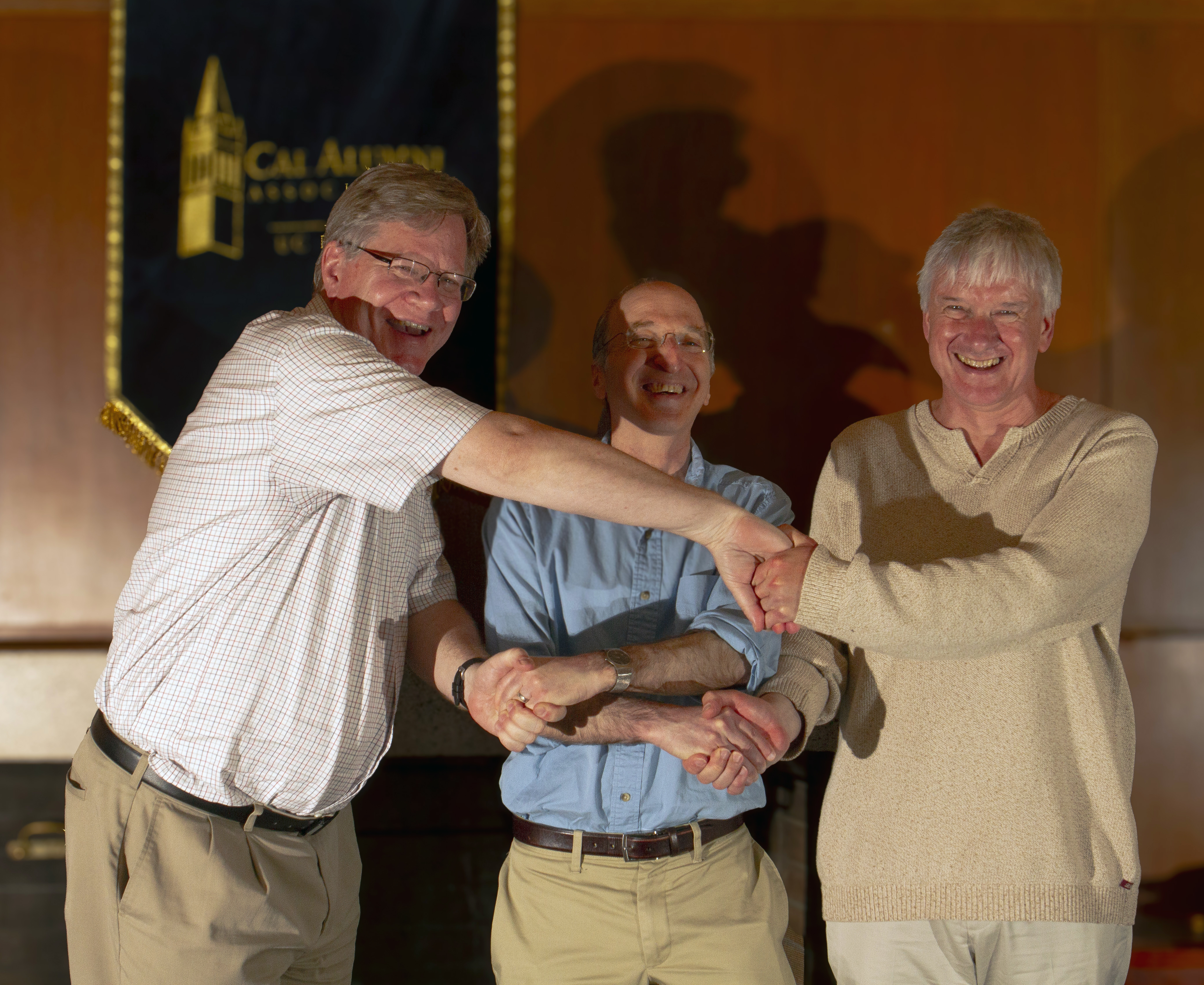 three smiling men linking arms in celebration
