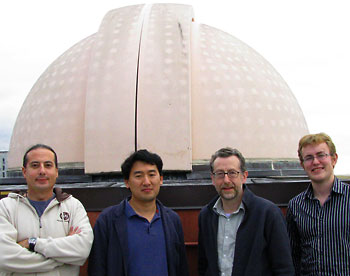 Four people stand in front of a large telescope.