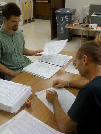 Three people examine papers at a table.