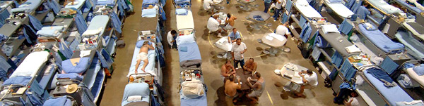 Rows of blue bunkbeds and many inmates crowded in a small area.
