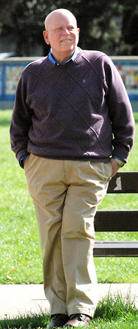Krisberg stands in a field wearing a brown sweater and khakis.