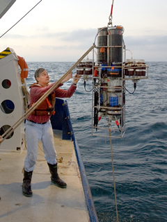 A man standing on a boat uses a pulley system to pull up a five-foot long metal object from the water.