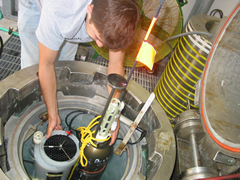 A man places a pump and wires inside a large metal cylinder.