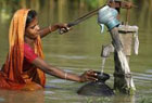Woman standing in waist deep water filling plate from well.