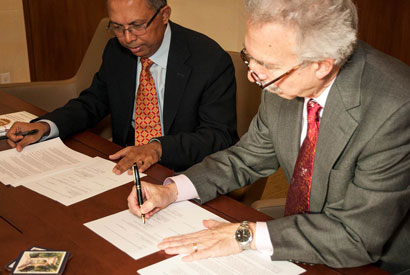 Subir Chowdhury and Nicholar Dirks sitting at table with documents in front of them.  Dirks is signing a document.