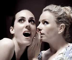 Stock photo of two women whispering.