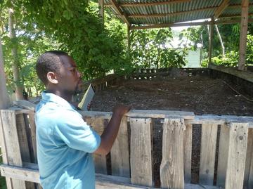 A man in a blue polo shirt stands in front of a covered box of composting organic material