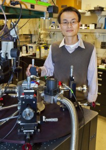 Peidong Yang stands in a lab with a very large microscope.