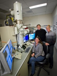 Three researchers stand in front of a system of computers and microscopes.