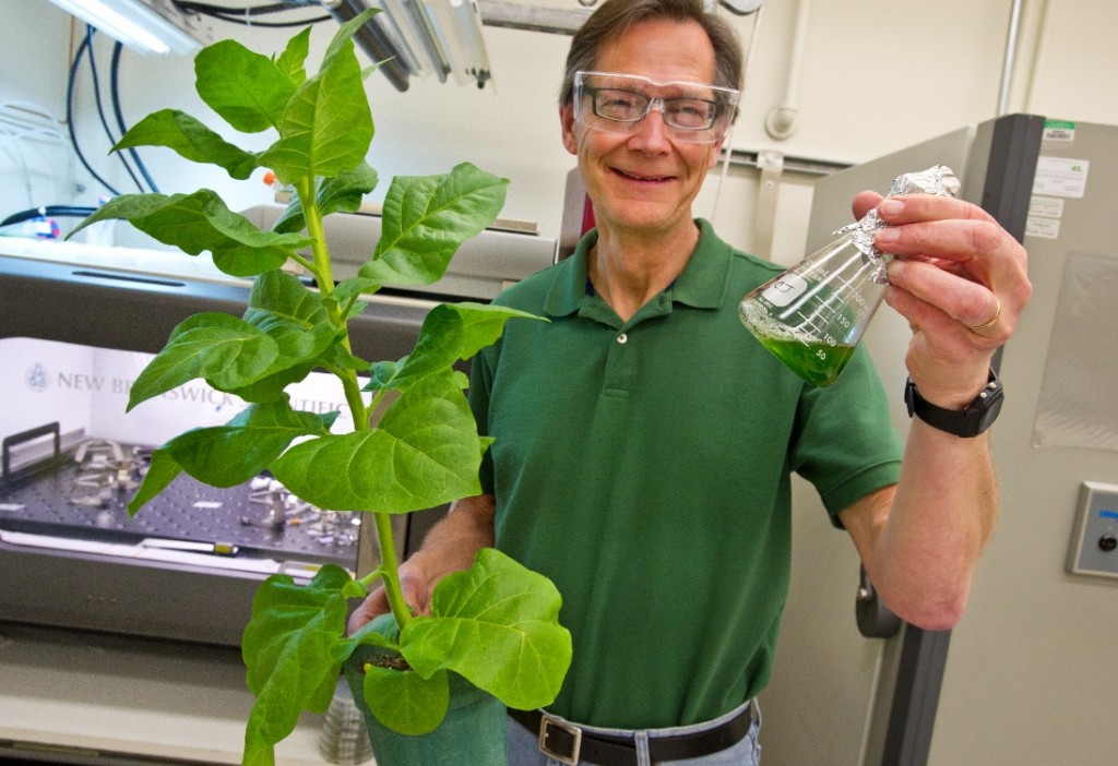 Jansson holds a plant in one hand and a flask of green liquid in the other.