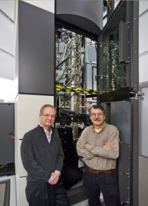 Two researchers standing in front of a large microscope.