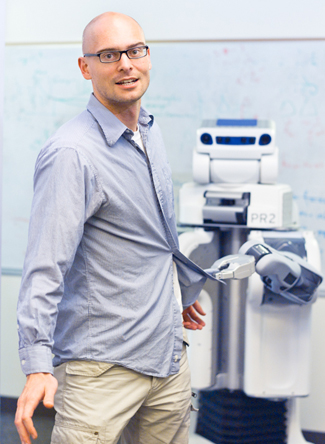 Abbeel poses with a robot tugging on his shirt.