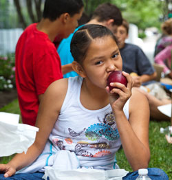 Girl biting into a fruit.
