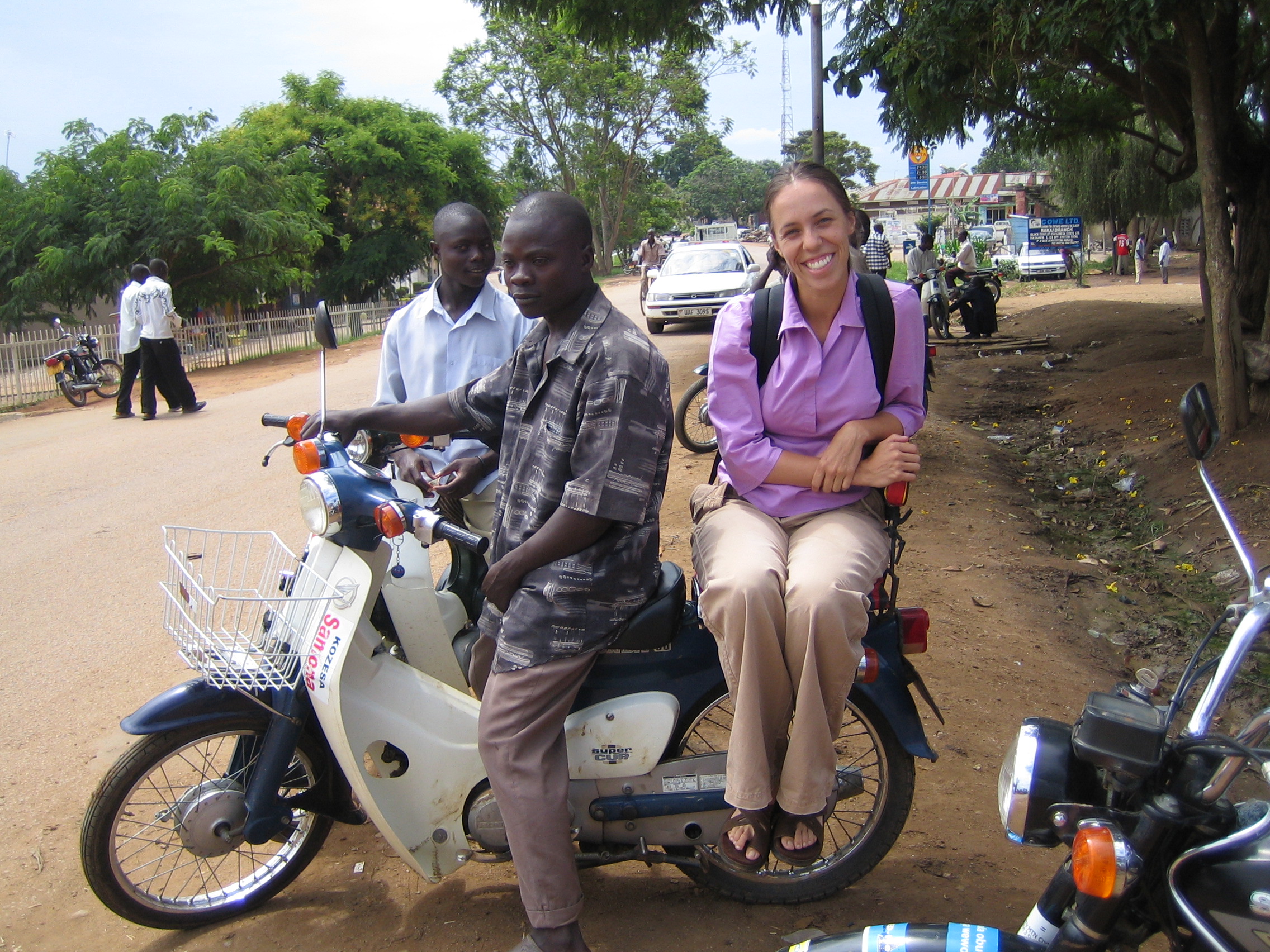 Burrell rides on the back of a Ugandan man's motorcycle.