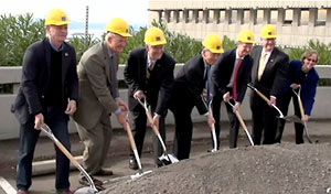 men in suits and hardhats work the ground with hoes.