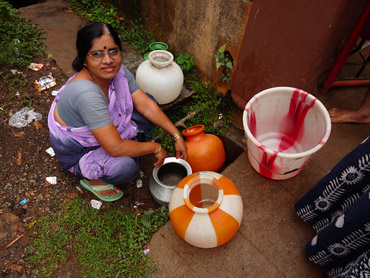 A woman in a sari attempts to fill buckets at a well.