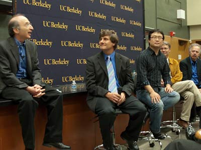 Five men sit in a panel speaking to an audience.
