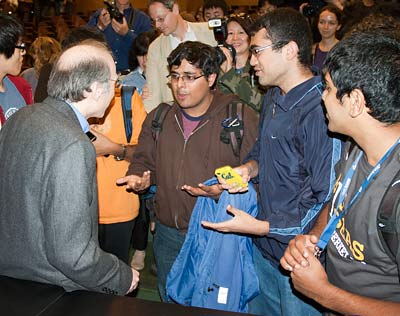 Three teenage boys speak with Perlmutter amid a large crowd of students.