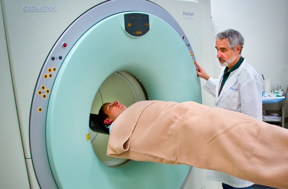 Man standing next to person entering a CT scanner 