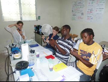 Four people, Gabrielle Pecora, Sasha Kramer, Jean Marie Noel, and Jimmy Louis sit around a table covered in lab equipment while extracting DNA using micro-pipettes
