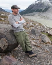 Professor Kurt Cuffey leaning against a boulder at a remote mountain location in Patagonia.
