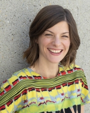 Associate professor Desiree Fields, smiling, wearing a colorfully patterned blouse in front of grey concrete background.